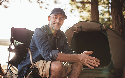 Photo of a senior man at a campground with his tent in the background.